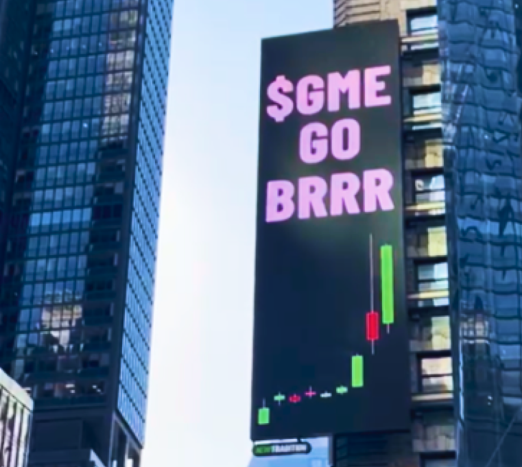 Digital billboard displaying the phrase '$GME GO BRRR' in pink letters, with a stock chart graphic below, positioned on a high-rise building facade in a cityscape. The message references the GameStop stock surge.
