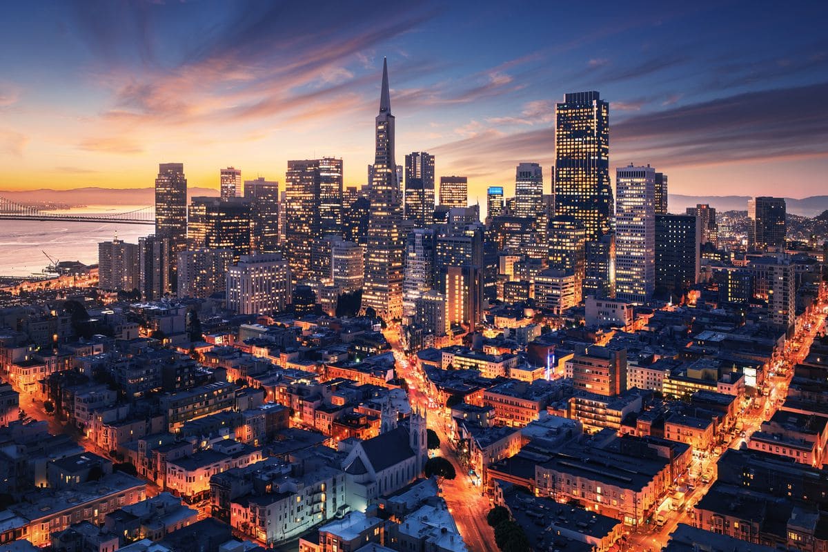 San Francisco skyline at dusk, showcasing illuminated skyscrapers and a view of the Transamerica Pyramid against a colorful sunset.